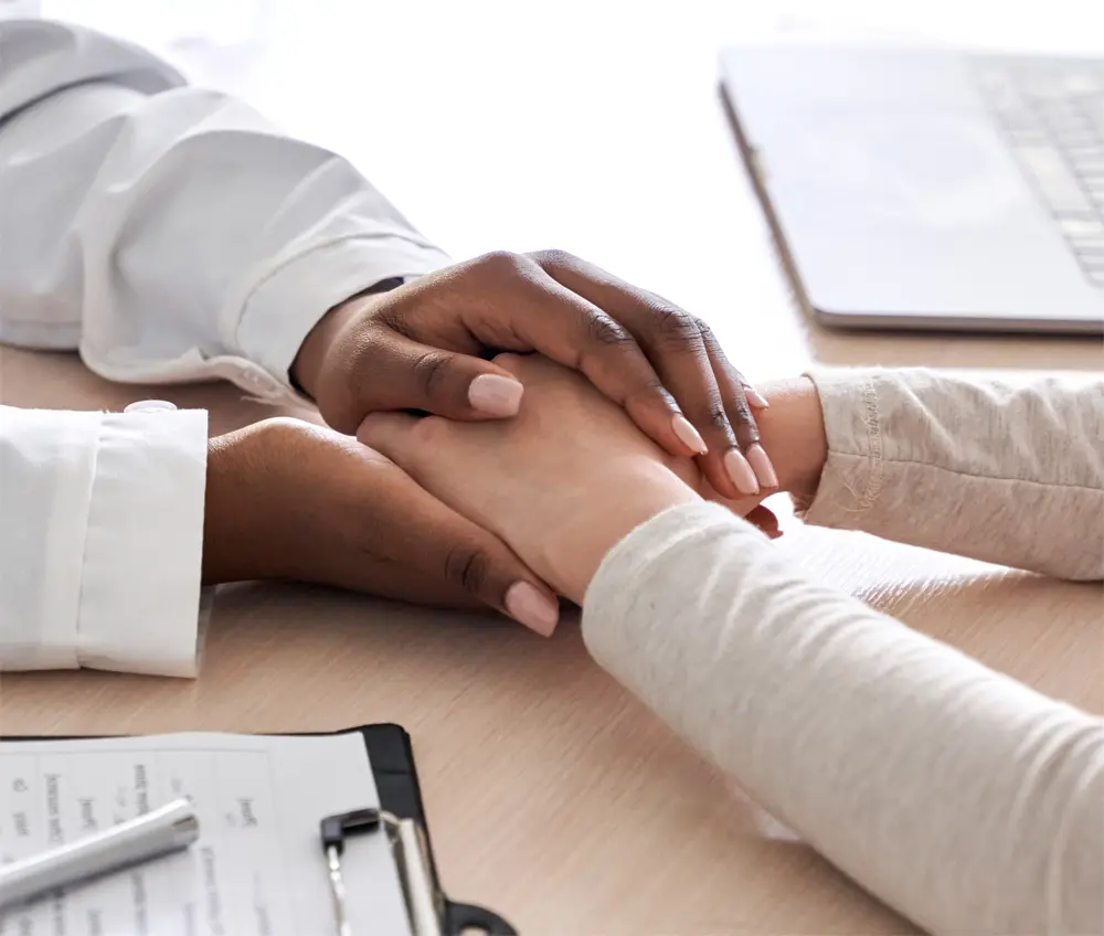 Close-up of a doctor comforting a patient by holding hands over a clinic desk