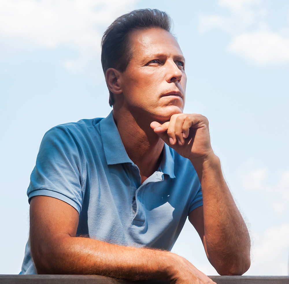 Middle-aged man in a blue polo shirt looking thoughtfully into the distance with his hand on his chin.